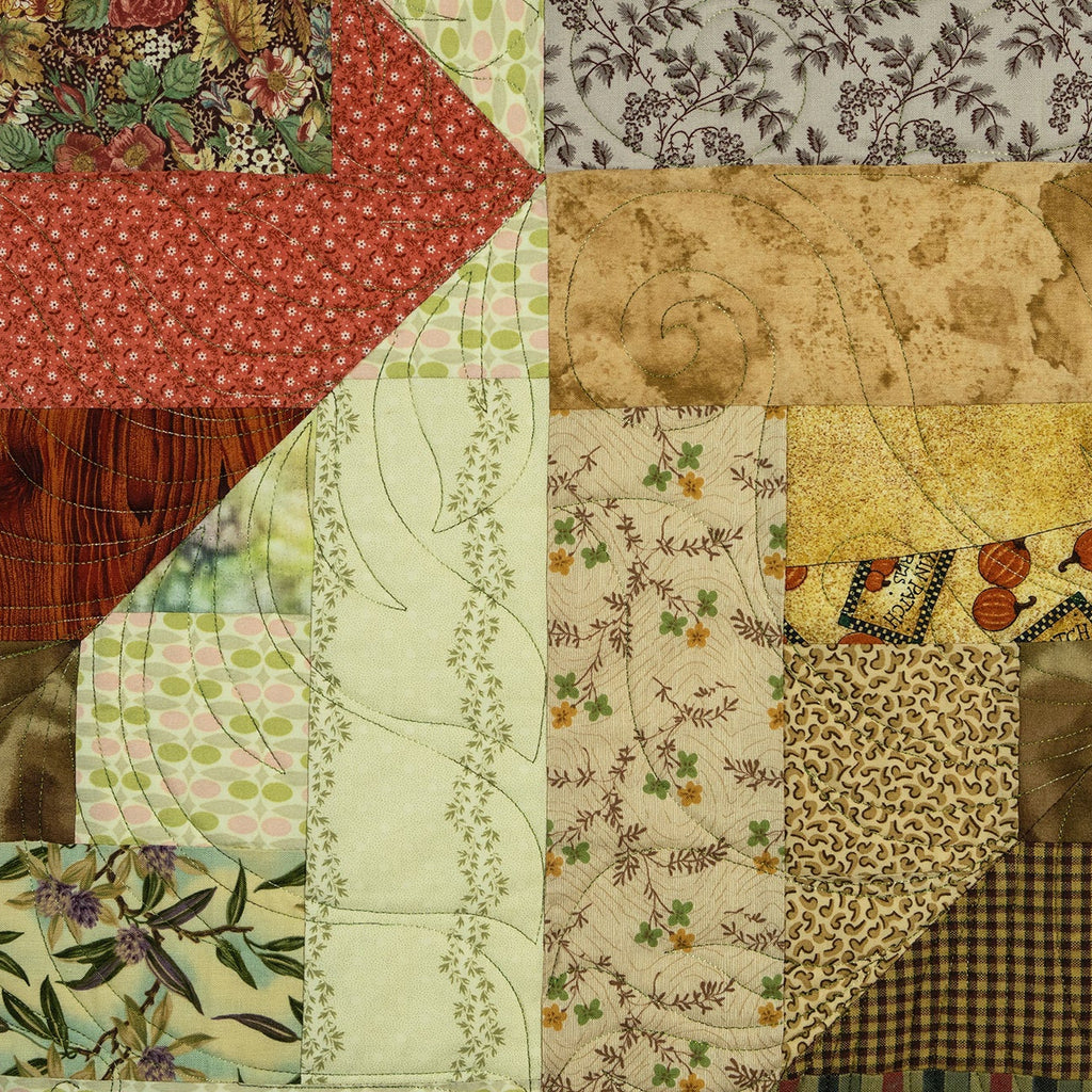 A close-up of a patchwork quilt featuring multiple fabric panels with different patterns, including floral, paisley, checkered, and textured prints in earthy tones of red, green, beige, brown, and yellow.
