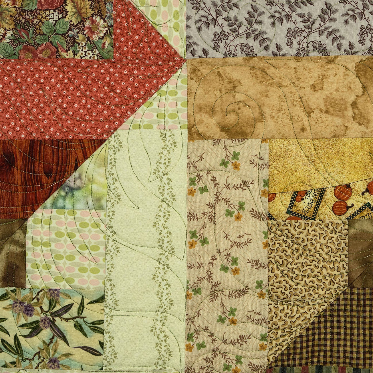 A close-up of a patchwork quilt featuring multiple fabric panels with different patterns, including floral, paisley, checkered, and textured prints in earthy tones of red, green, beige, brown, and yellow.