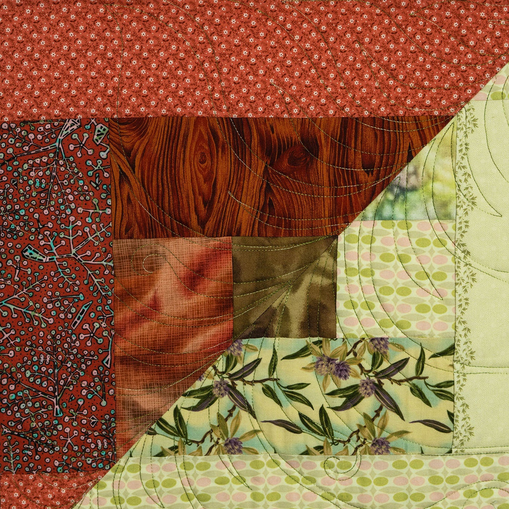 A close-up of a patchwork quilt featuring multiple fabric patterns, including red apple print, red floral fabric, brown wood grain, green and pink polka dots, and olive green leafy vines.