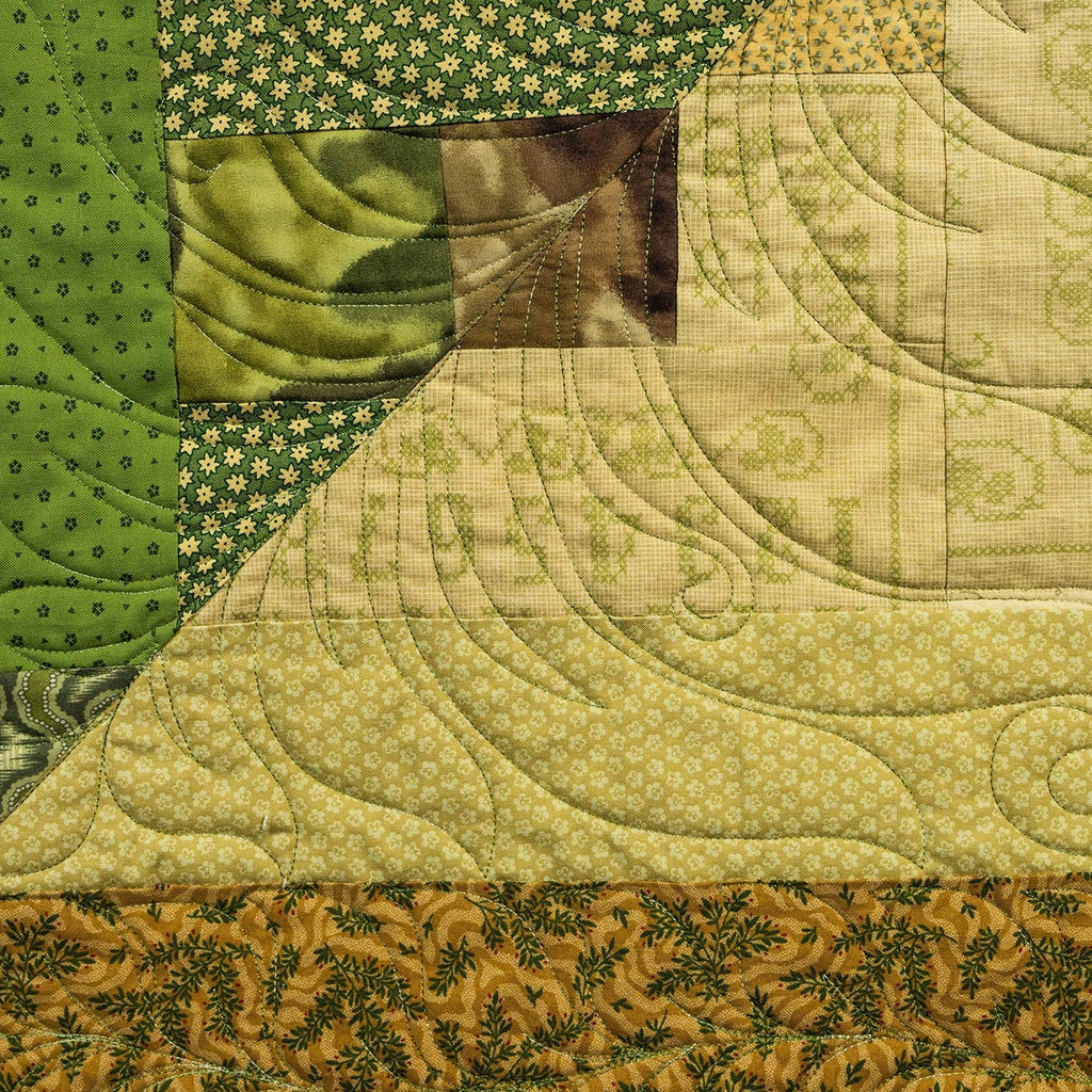 A close-up of a handmade quilted fabric panel featuring various patchwork patterns, including green polka dots, a floral print, and a central patch with a green leaf design.