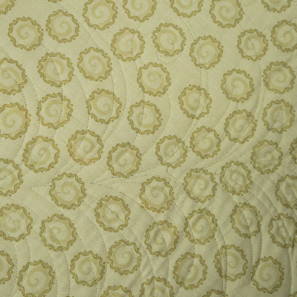 A close-up of a quilted fabric featuring a repeating pattern of circular medallions in olive green on a cream background.