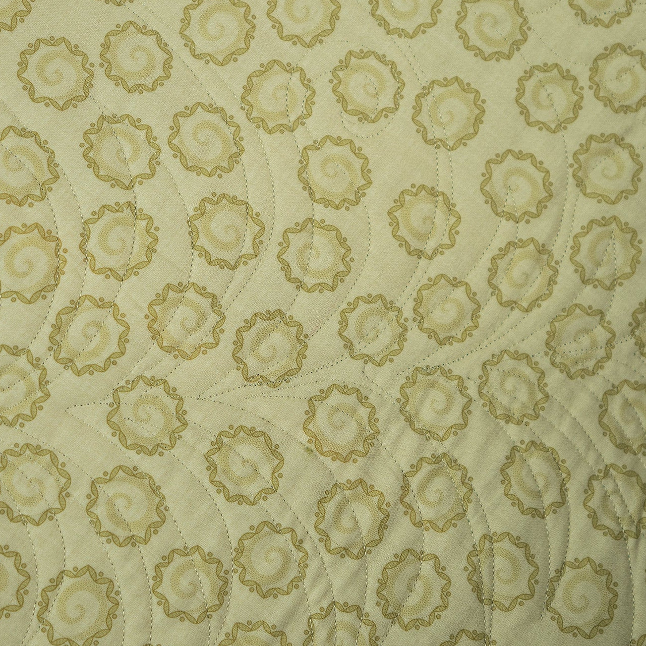 A close-up of a quilted fabric featuring a repeating pattern of circular medallions in olive green on a cream background.