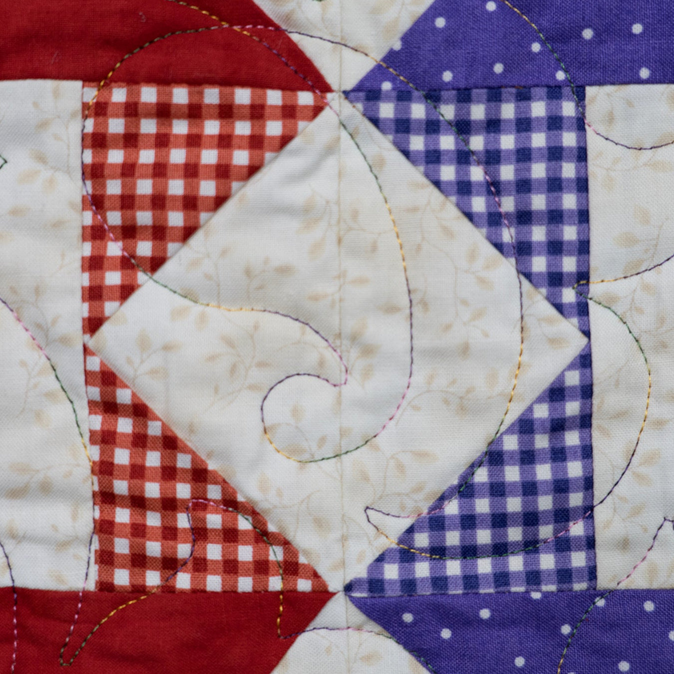 A close-up of a quilted fabric panel featuring a patriotic color-blocked design with red, white, and blue sections. The fabrics include solid red, red-and-white gingham, white with a subtle floral print, blue-and-white gingham, and blue with white polka dots.