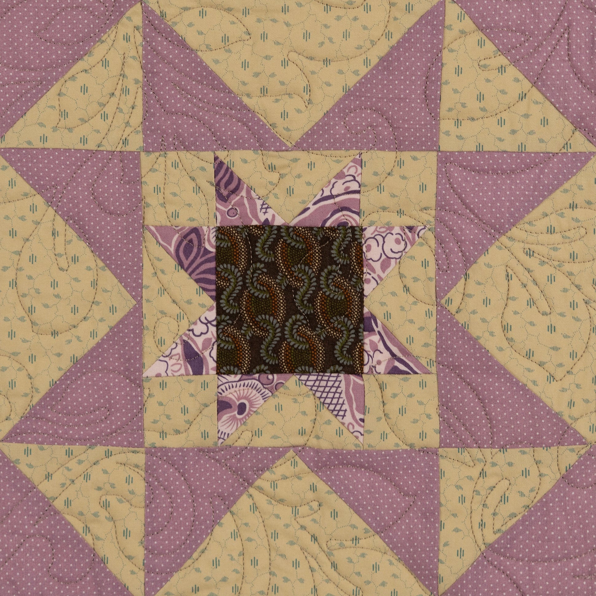 A square quilt block featuring a geometric star pattern with alternating lavender-purple and beige patterned triangles, surrounding a central dark brown paisley star.