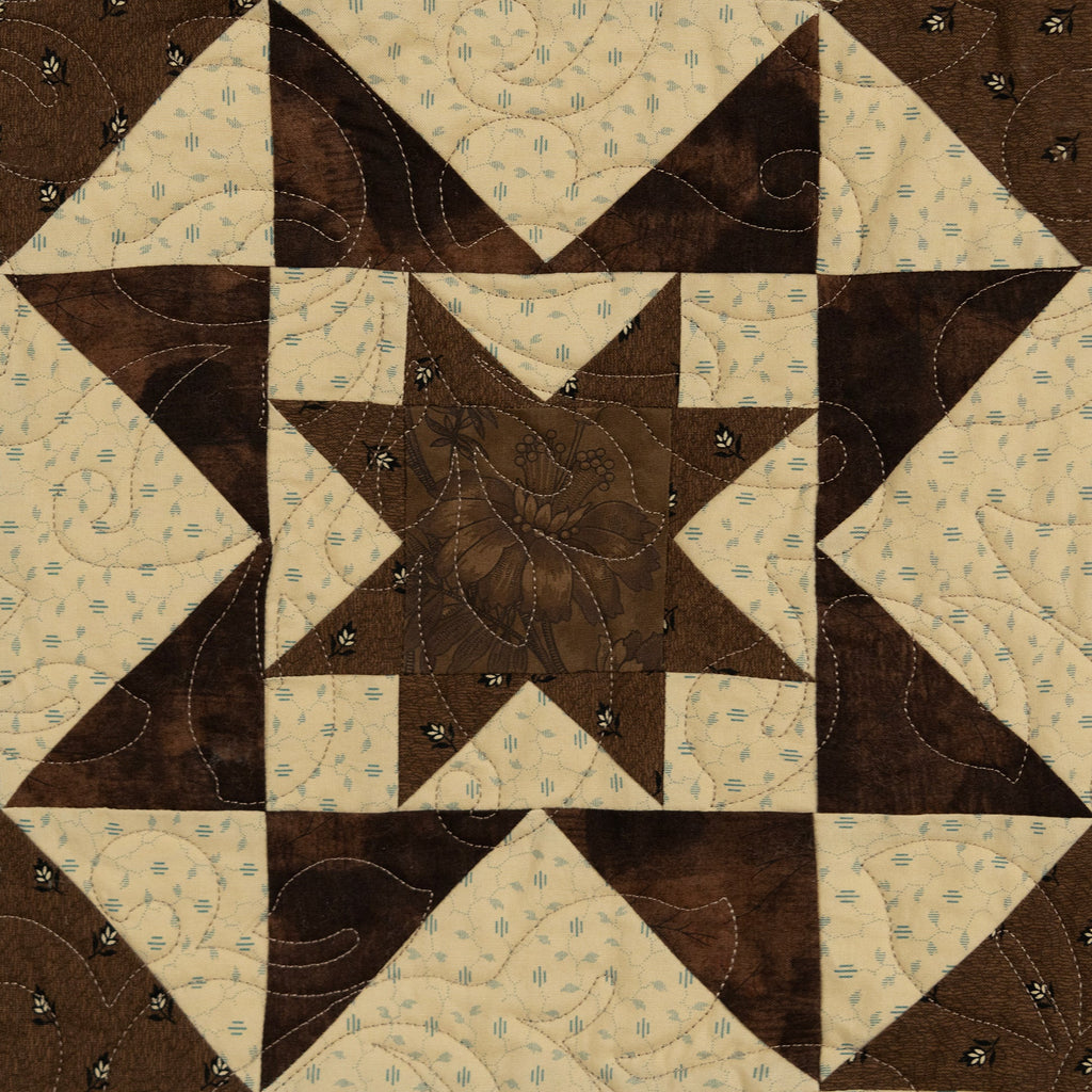 A square quilted patch featuring a geometric star and corner block pattern in dark brown and cream fabric with decorative quilting stitches.