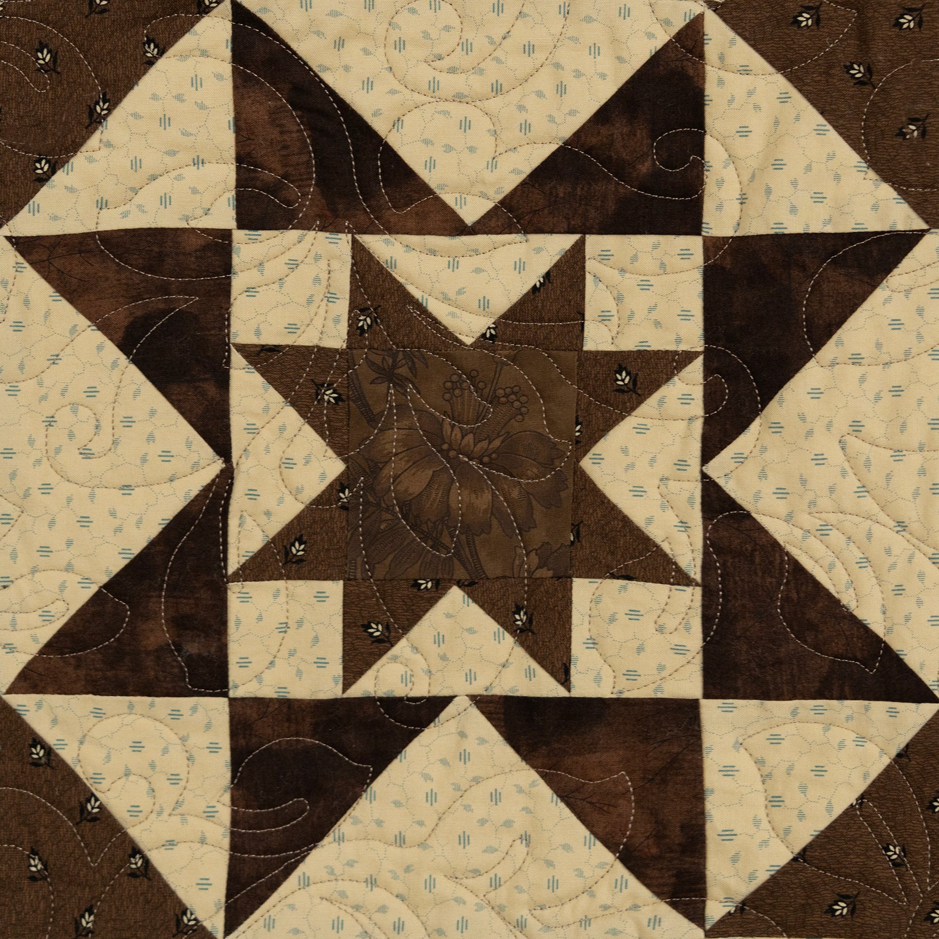 A square quilted patch featuring a geometric star and corner block pattern in dark brown and cream fabric with decorative quilting stitches.