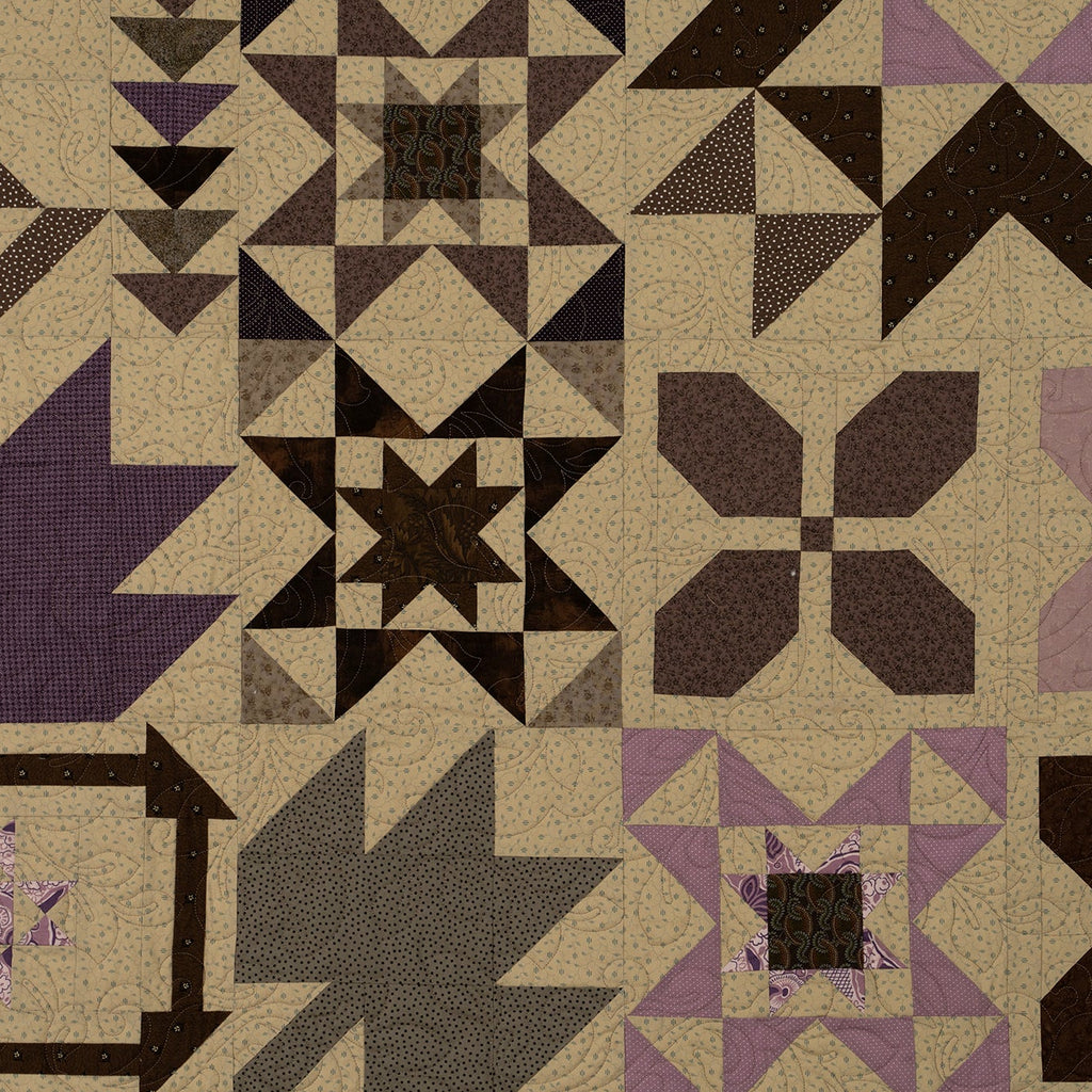 A quilted fabric panel featuring a patchwork design of geometric and floral starburst patterns in beige, dark brown, purple, and gray.