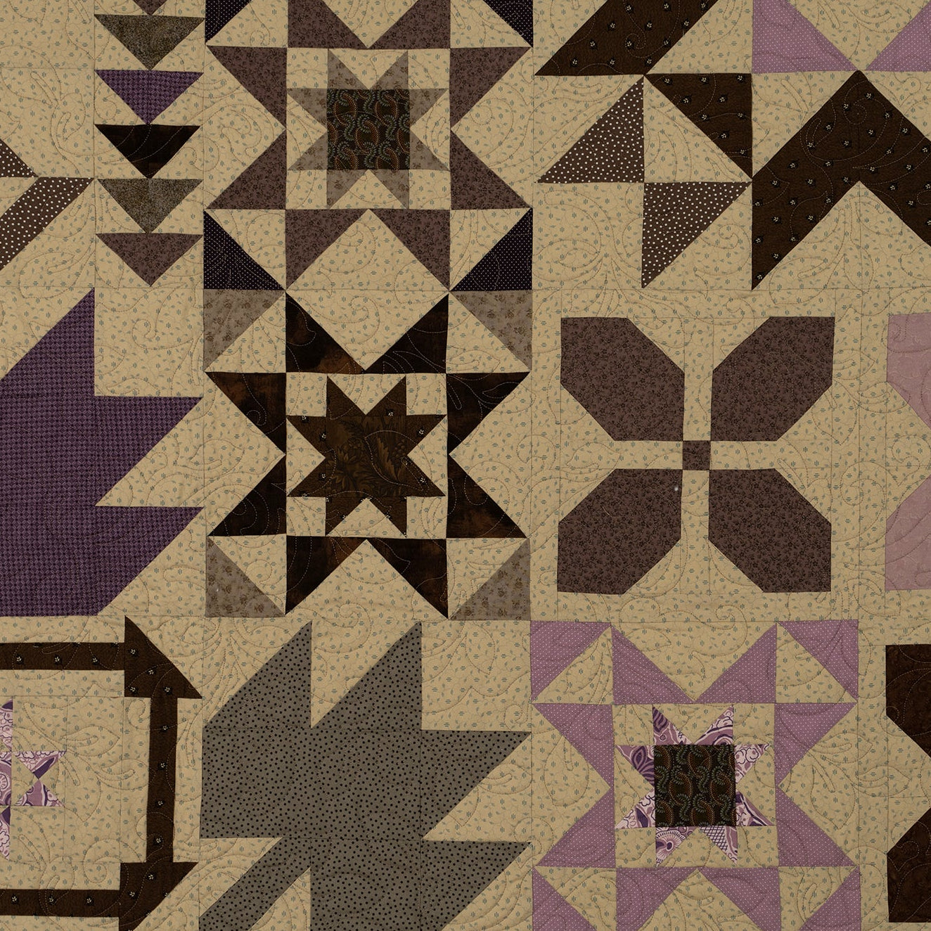 A quilted fabric panel featuring a patchwork design of geometric and floral starburst patterns in beige, dark brown, purple, and gray.