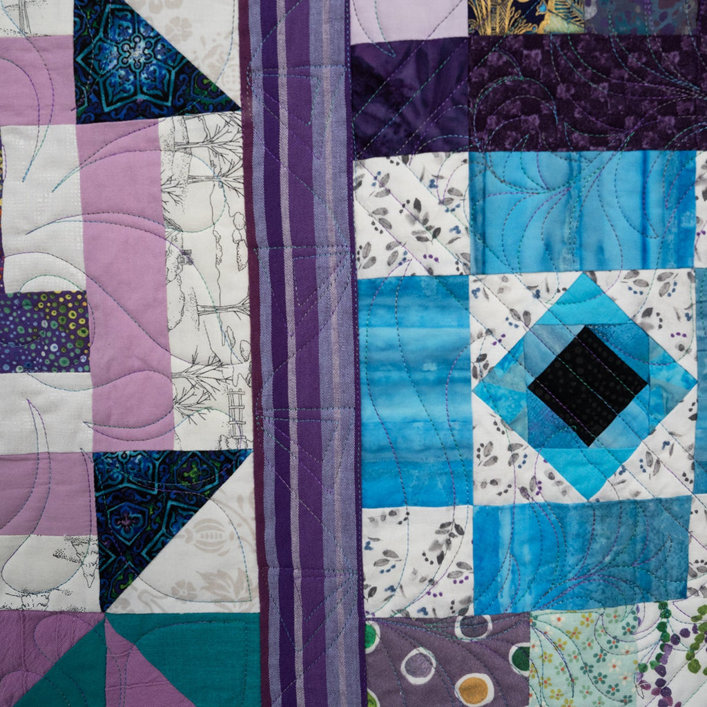 Colorful quilt with geometric patterns in purple, blue, and white.