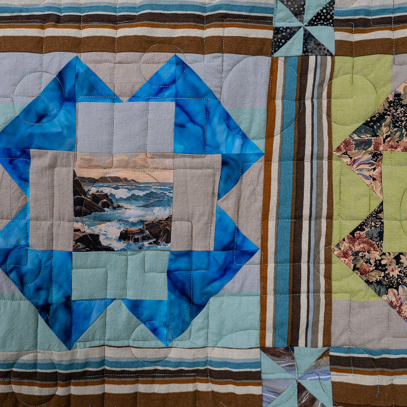 A close-up of a quilted patchwork textile featuring a central blue geometric star motif with a small landscape photo inset, surrounded by striped and floral fabric sections.