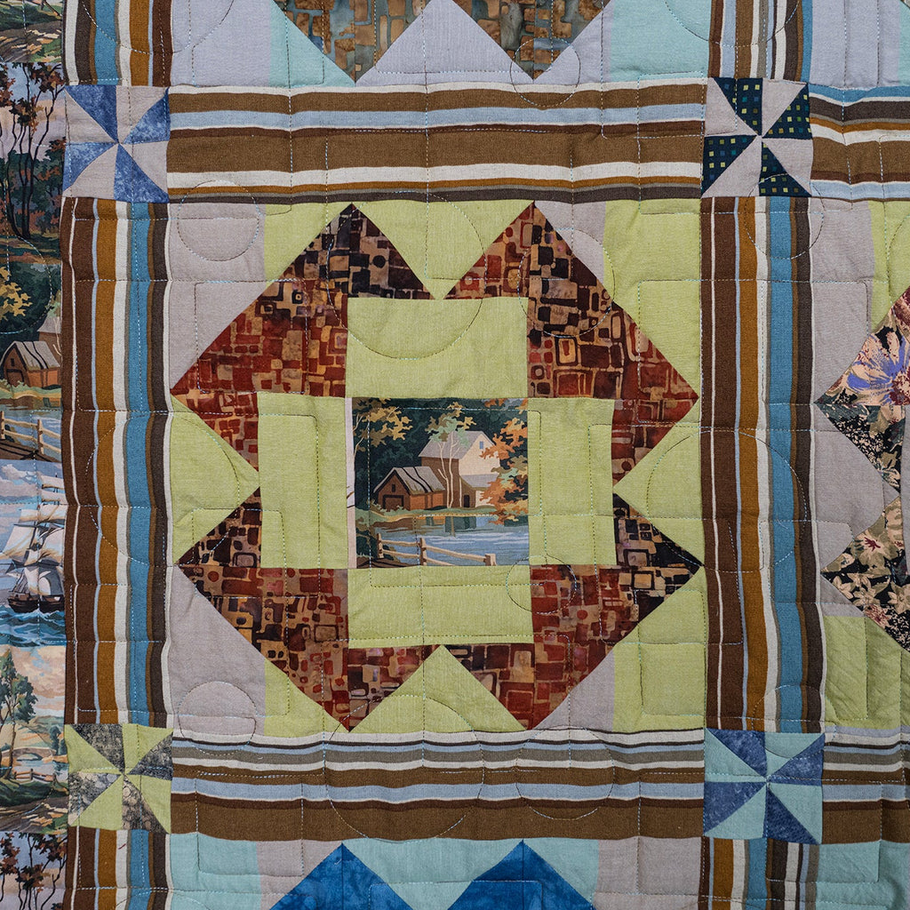 A close-up of a quilted patchwork textile featuring geometric and floral blocks in muted tones of beige, brown, blue, green, and cream, with small printed nature scenes visible in some sections.