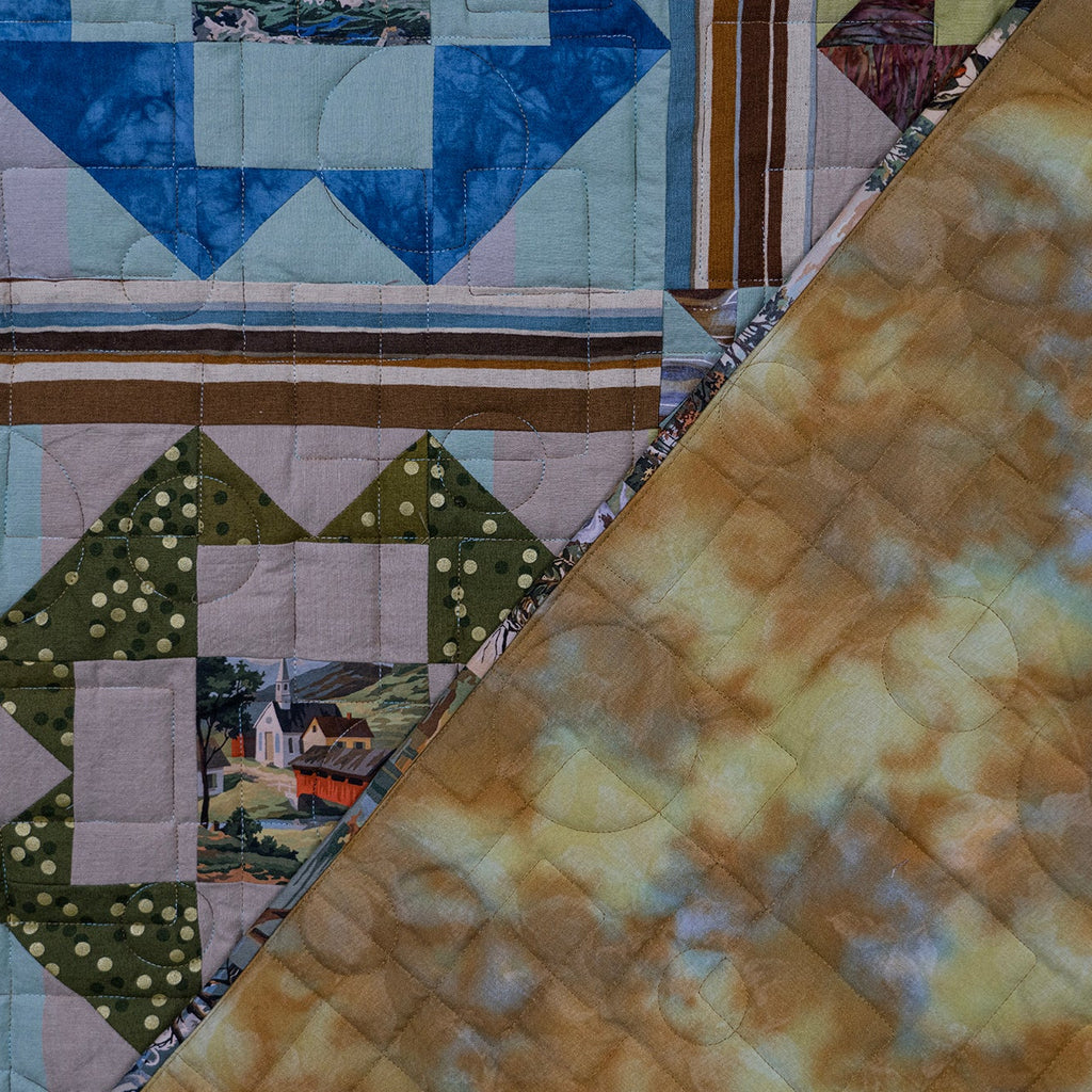 A close-up of a quilted textile with a diagonal split showing two different patterned sections: one side has a multicolor geometric and floral patchwork design, and the other side has a mottled tan, cream, and light blue fabric.
