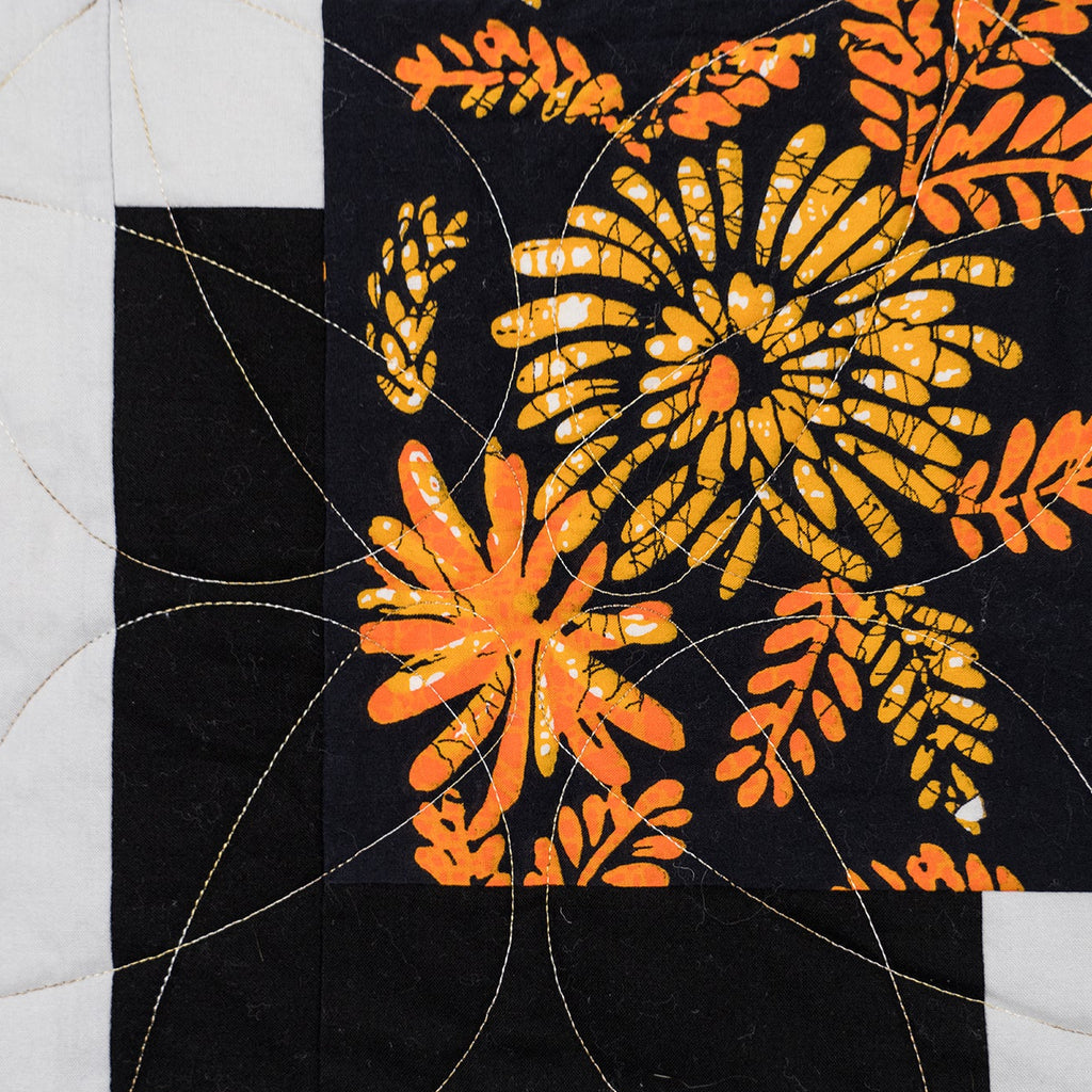 Quilt block with floral patterns in orange and black on a white background
