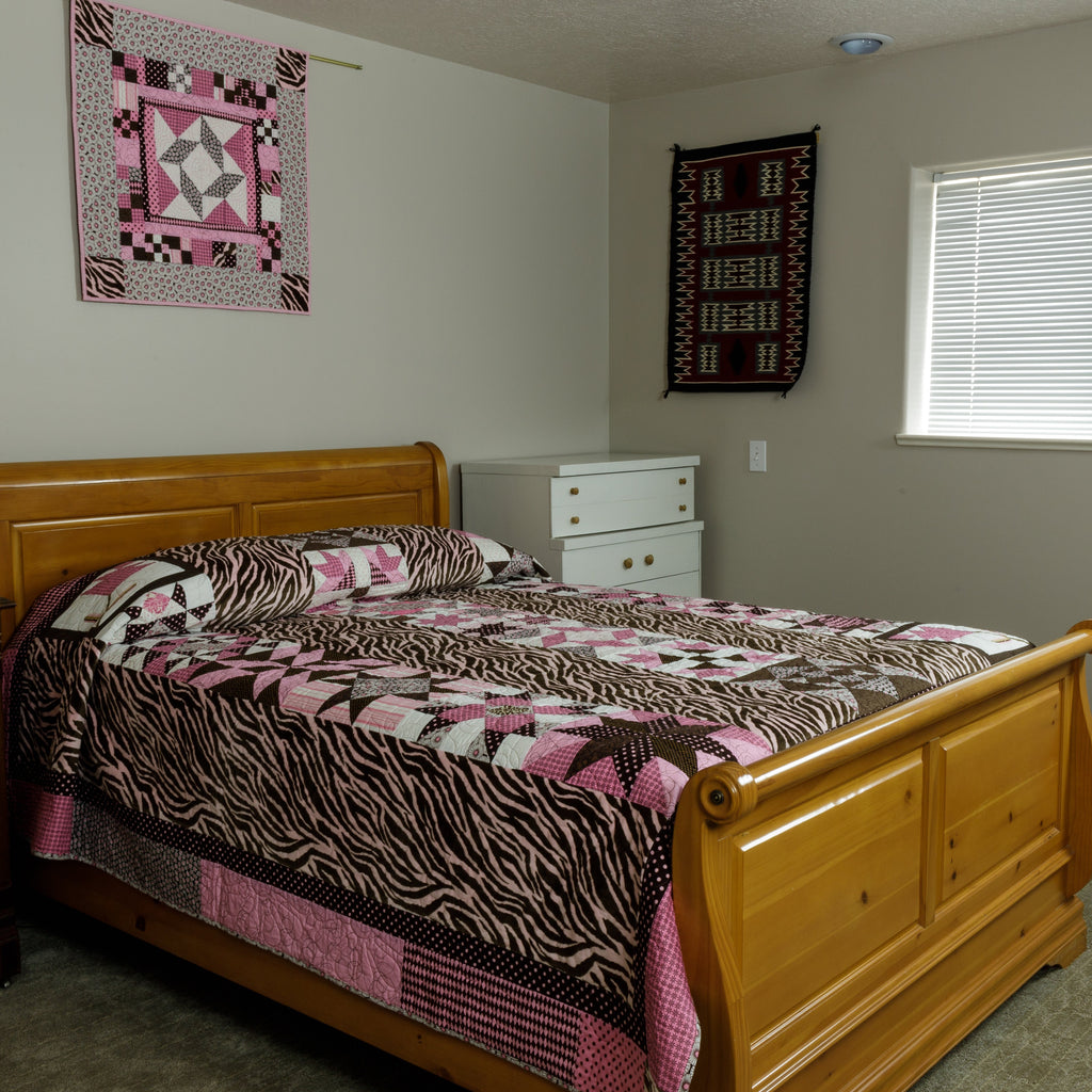 A hot pink and brown quilt and wall hanging in animal print laid out in a bedroom setting