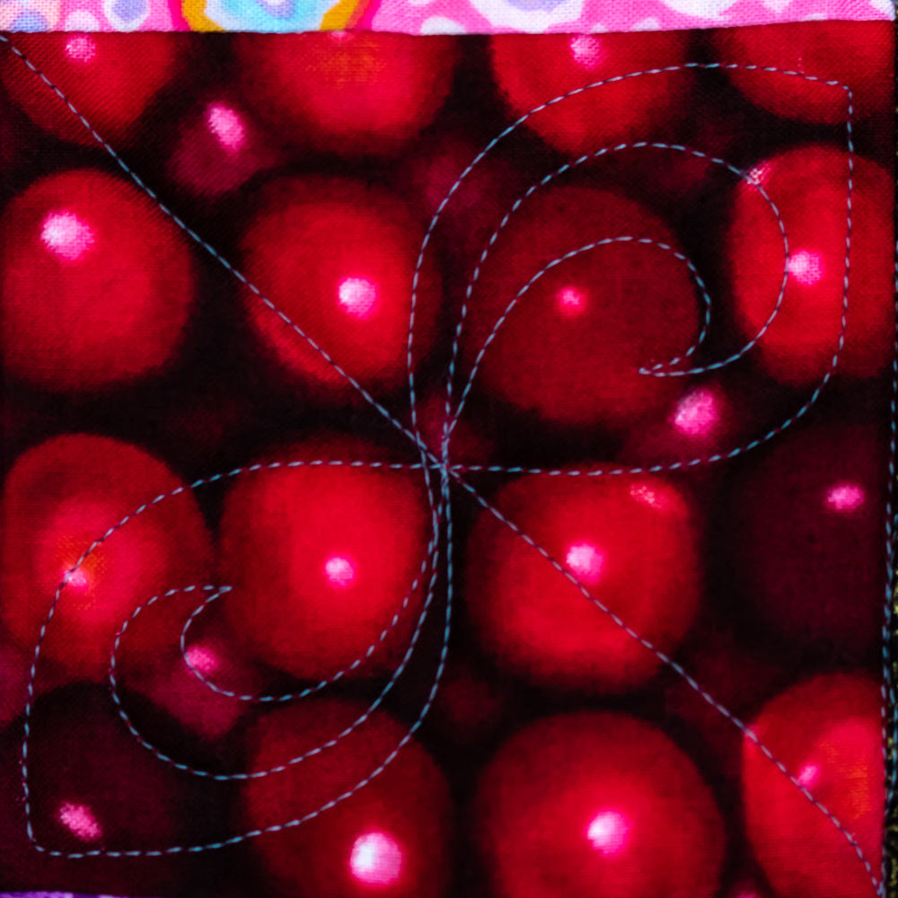 A close-up of a quilted fabric panel featuring a red pattern of glossy cherries with blue quilting stitches