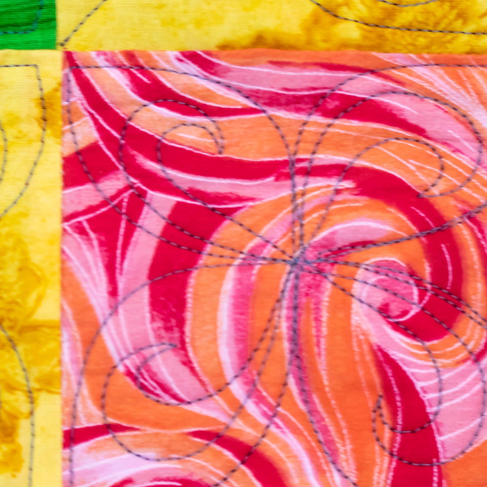 Close-up of a colorful quilted fabric with swirling abstract patterns in pink, red, orange, yellow, and blue, stitched with visible curved black and dashed quilting lines.
