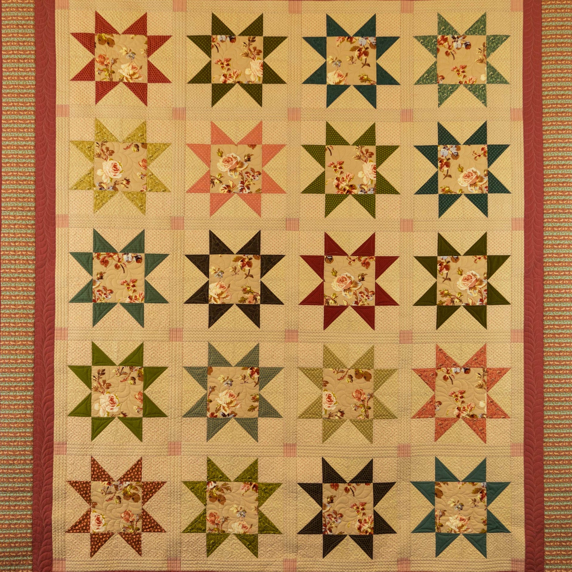 A vintage quilted star-patterned quilt hanging flat. The design features a grid of multi-colored star blocks with floral centers and striped borders in red, green, beige, and brown.