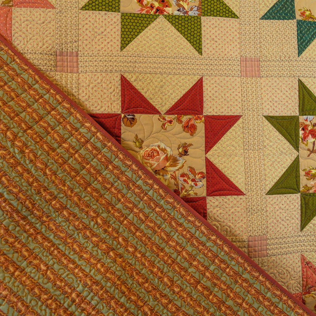 A close-up of a quilted textile showing a floral starburst pattern in red, green, and cream, with a striped reverse side in green, orange, and cream.