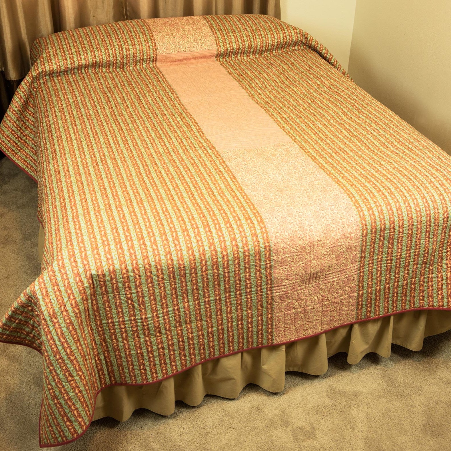 A striped quilted bedspread with a central solid panel, draped over a bed.