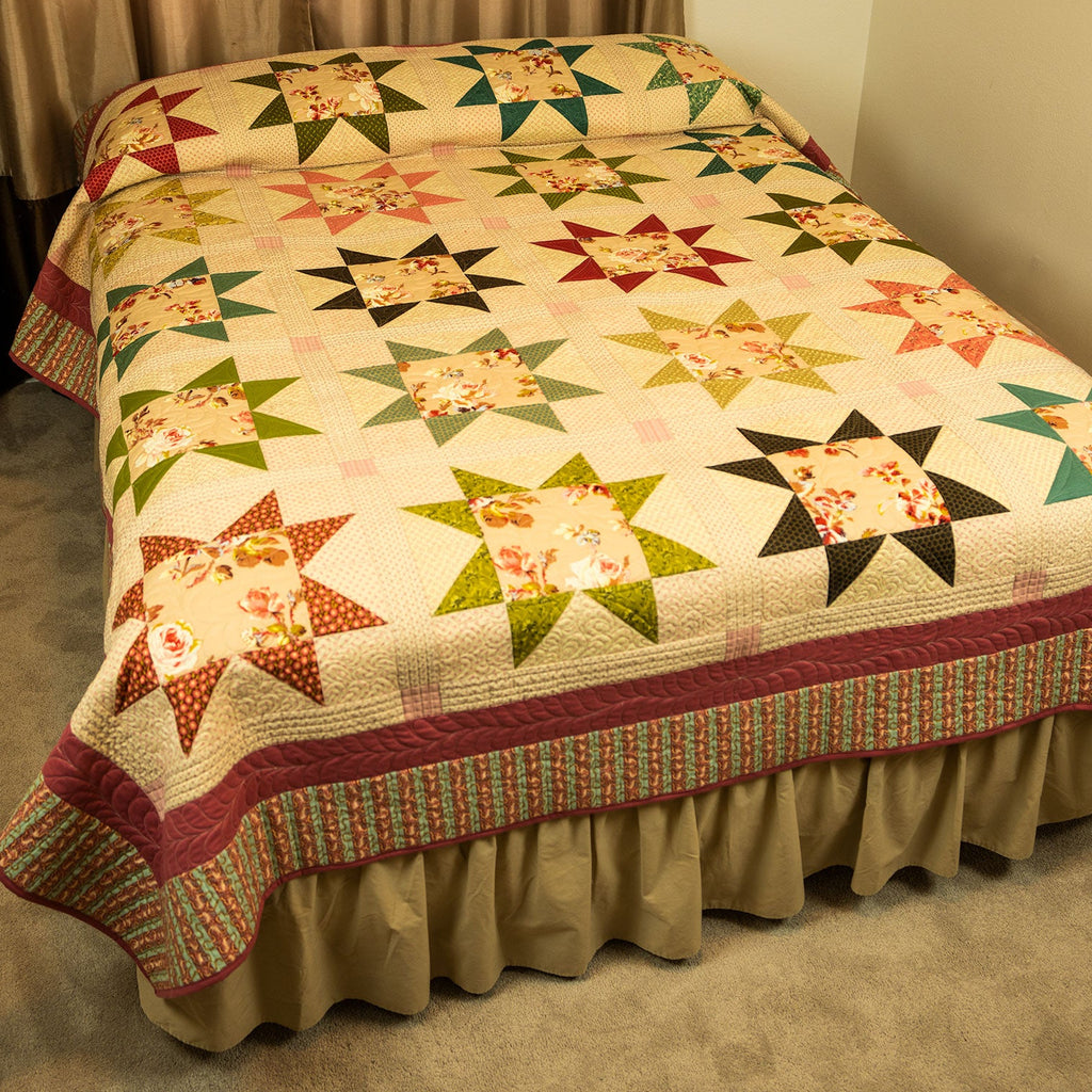 A quilted bedspread with a geometric star and floral block pattern, styled on a bed.