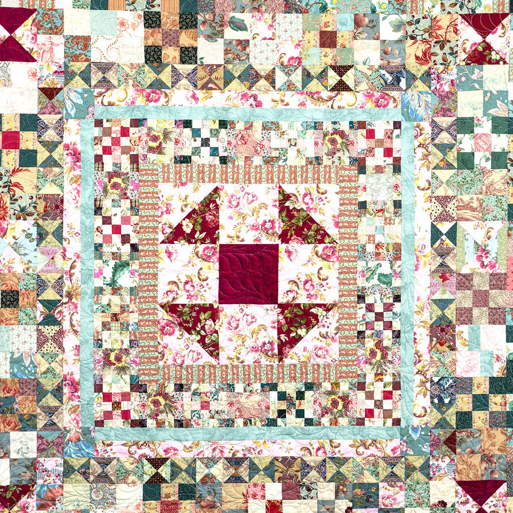 A square patchwork quilt with a central floral starburst design, surrounded by concentric borders of floral, geometric, and striped fabric blocks in muted pink, beige, green, and red tones.