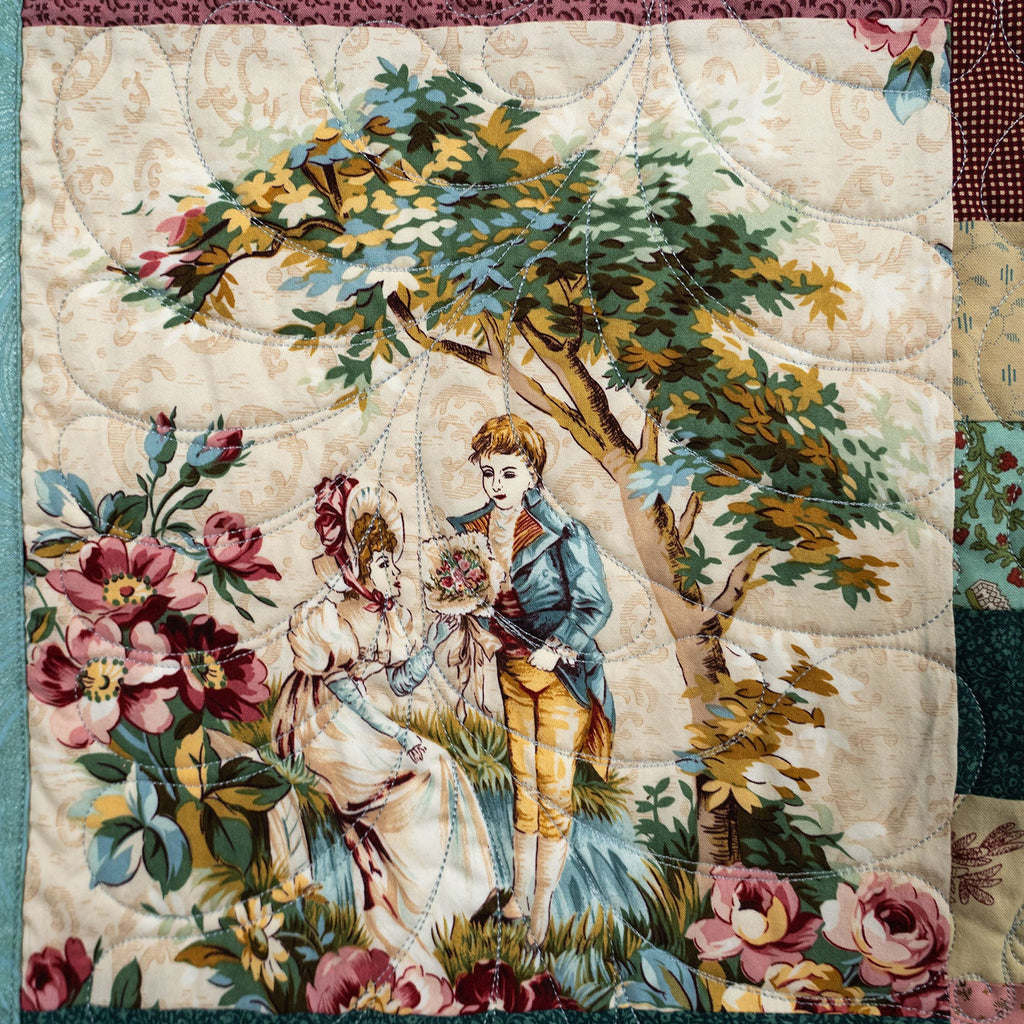 A vintage-style quilted textile featuring a central printed scene of a young couple under a leafy tree with flowers, alongside patchwork blocks of floral and paisley fabrics on the right side.