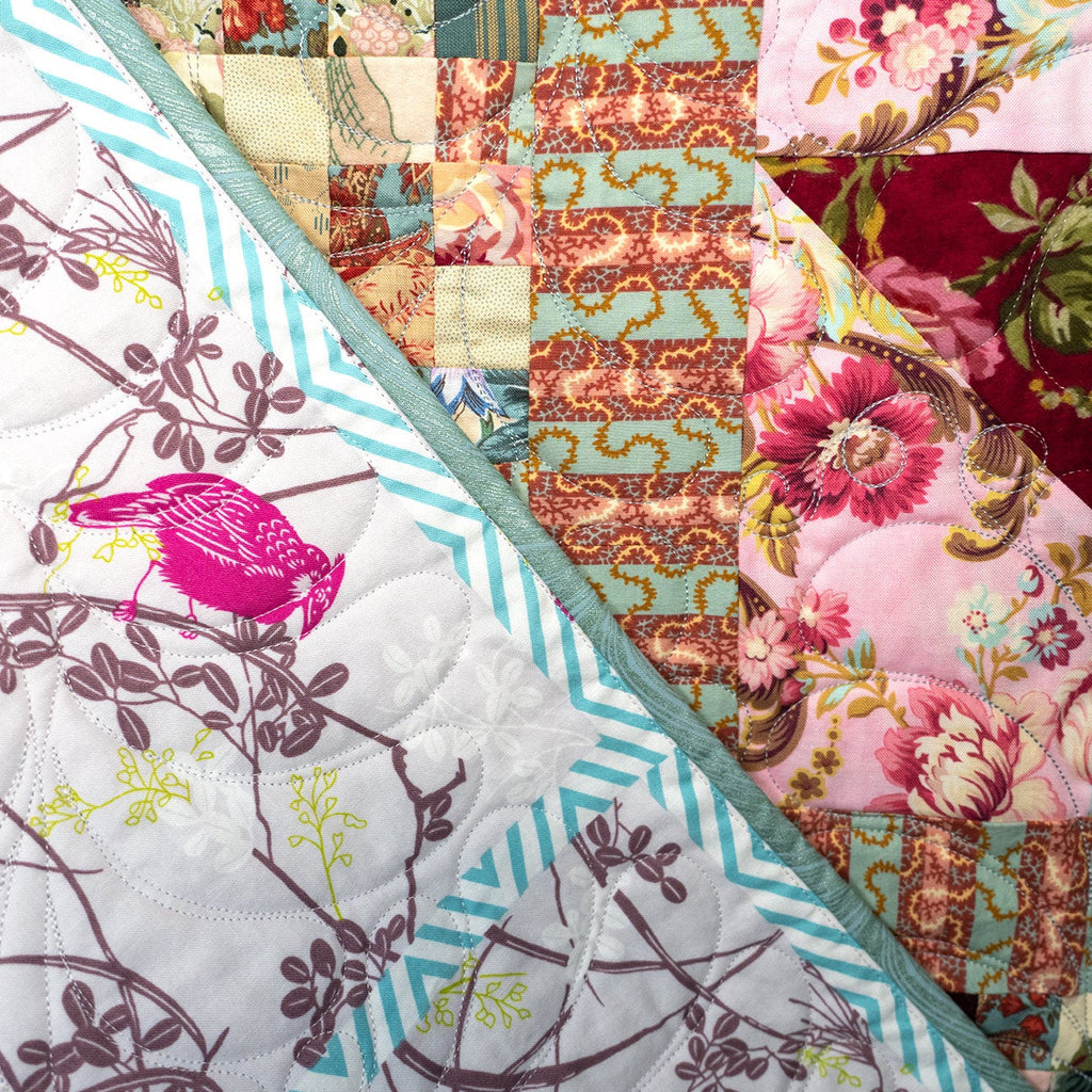 A close-up of a quilted fabric panel showing multiple patterned sections: a white section with pink birds and brown branch outlines, a pink floral section, a teal-and-white striped border, and a rust-brown patterned section.
