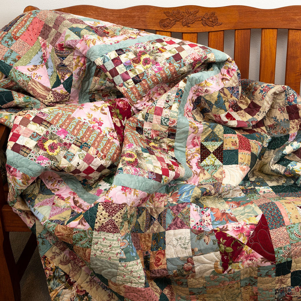 A patchwork quilt with a multicolor floral and geometric pattern draped over a wooden bench.