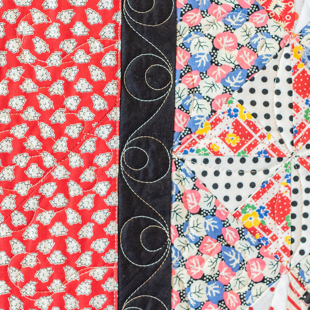Quilt with various patterns including red floral, black scrollwork, and multicolored geometric designs.