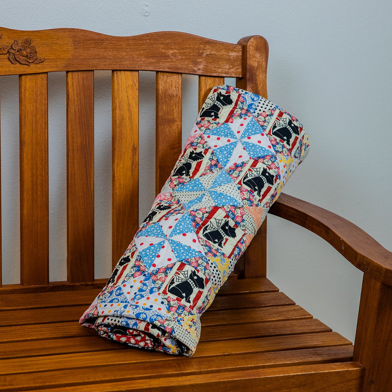 Colorful quilt with black and white dog pattern draped over a wooden bench against a plain wall.