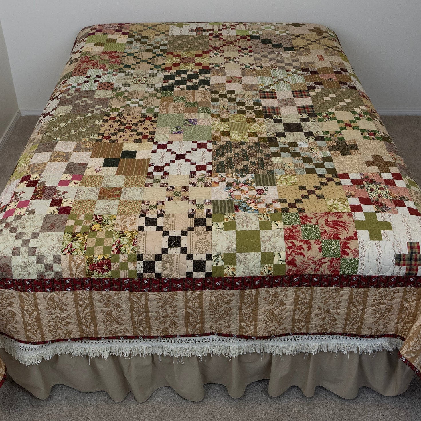 Patchwork quilt on a bed in a room with plain walls and floor.