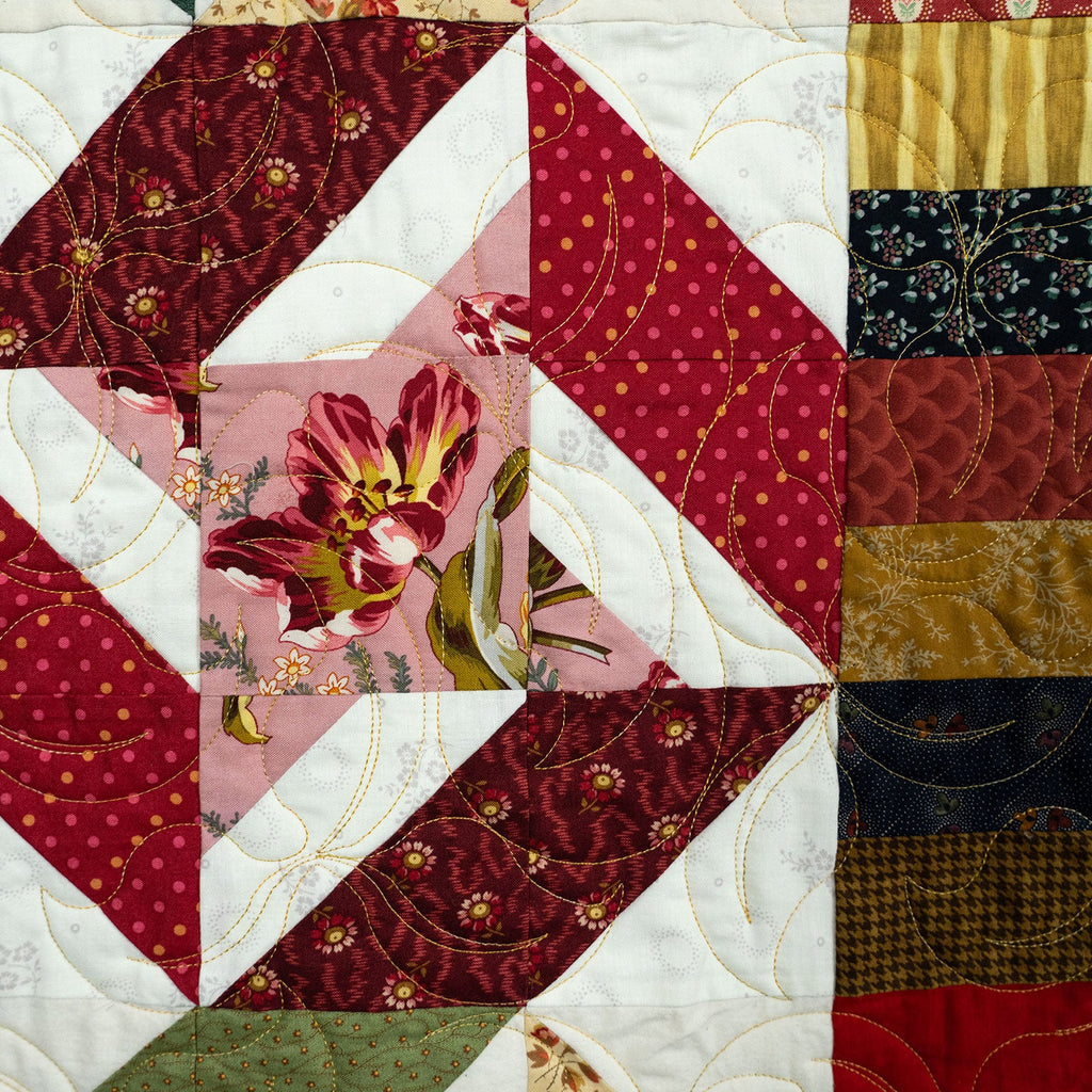 Quilt with floral and geometric patterns in red, pink, and gold.