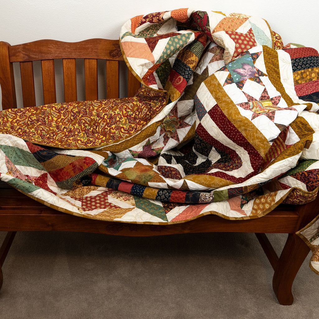 Colorful quilt draped over a wooden bench against a neutral background