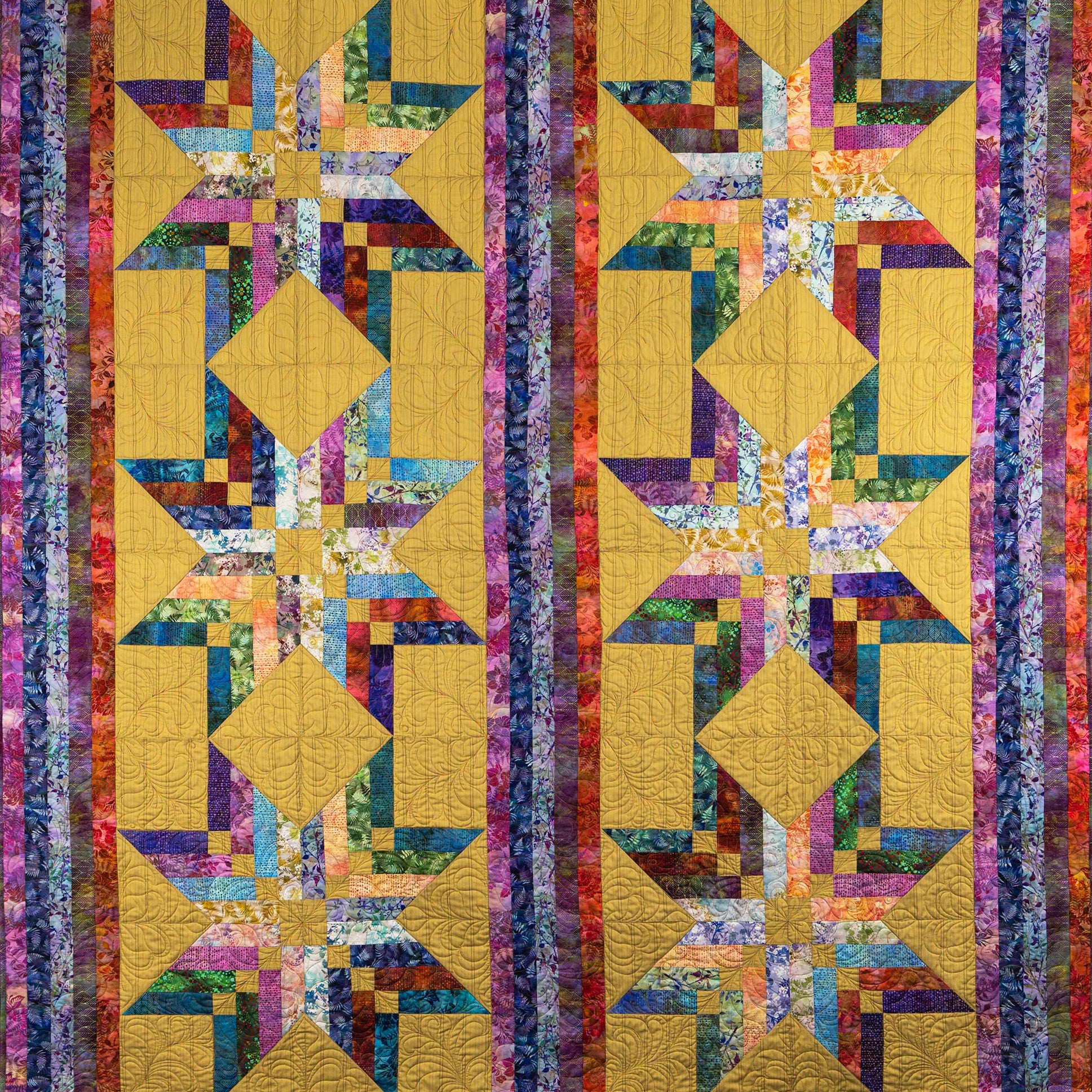 A square quilted textile featuring a repeating geometric star and diamond pattern in mustard yellow, purple, blue, green, pink, and orange, bordered by vertical multicolored patterned stripes.