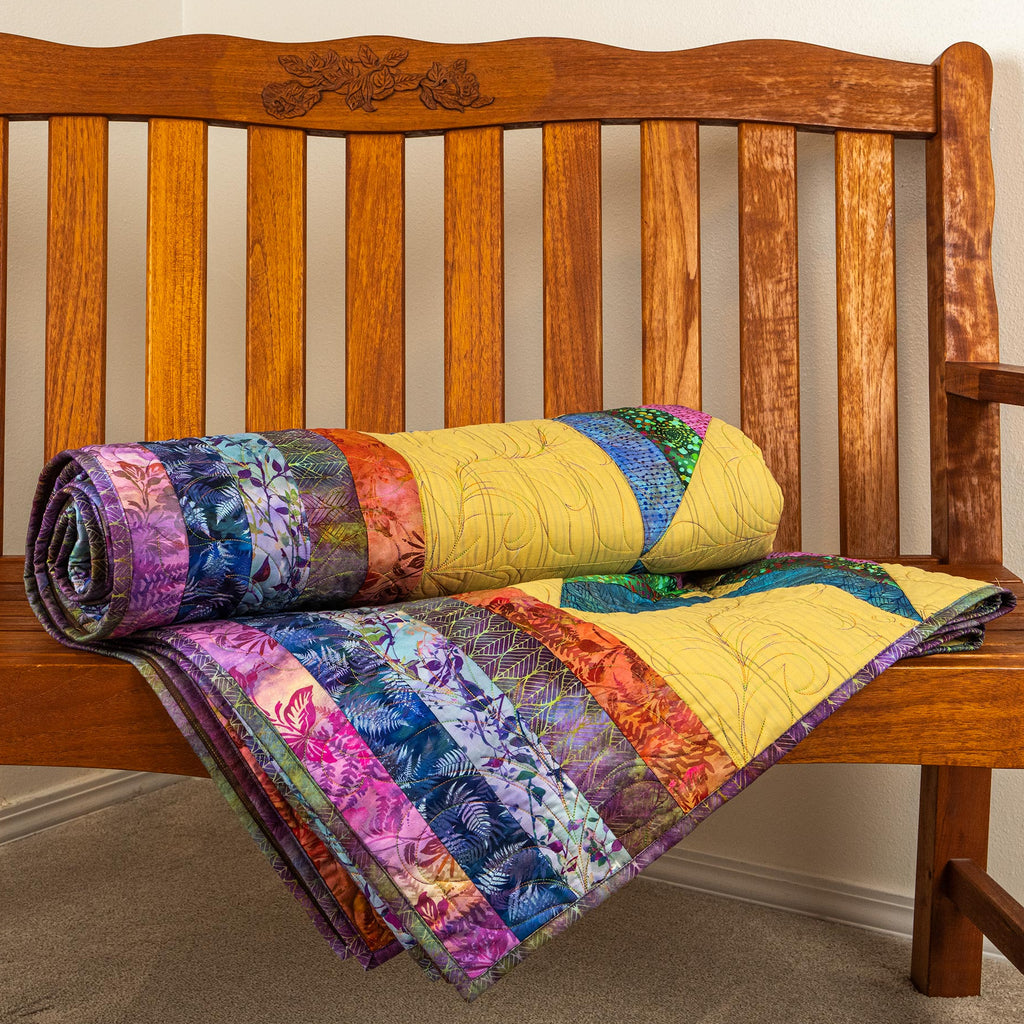 A colorful patchwork quilt with floral and striped patterns, rolled up and draped over a rustic wooden bench.
