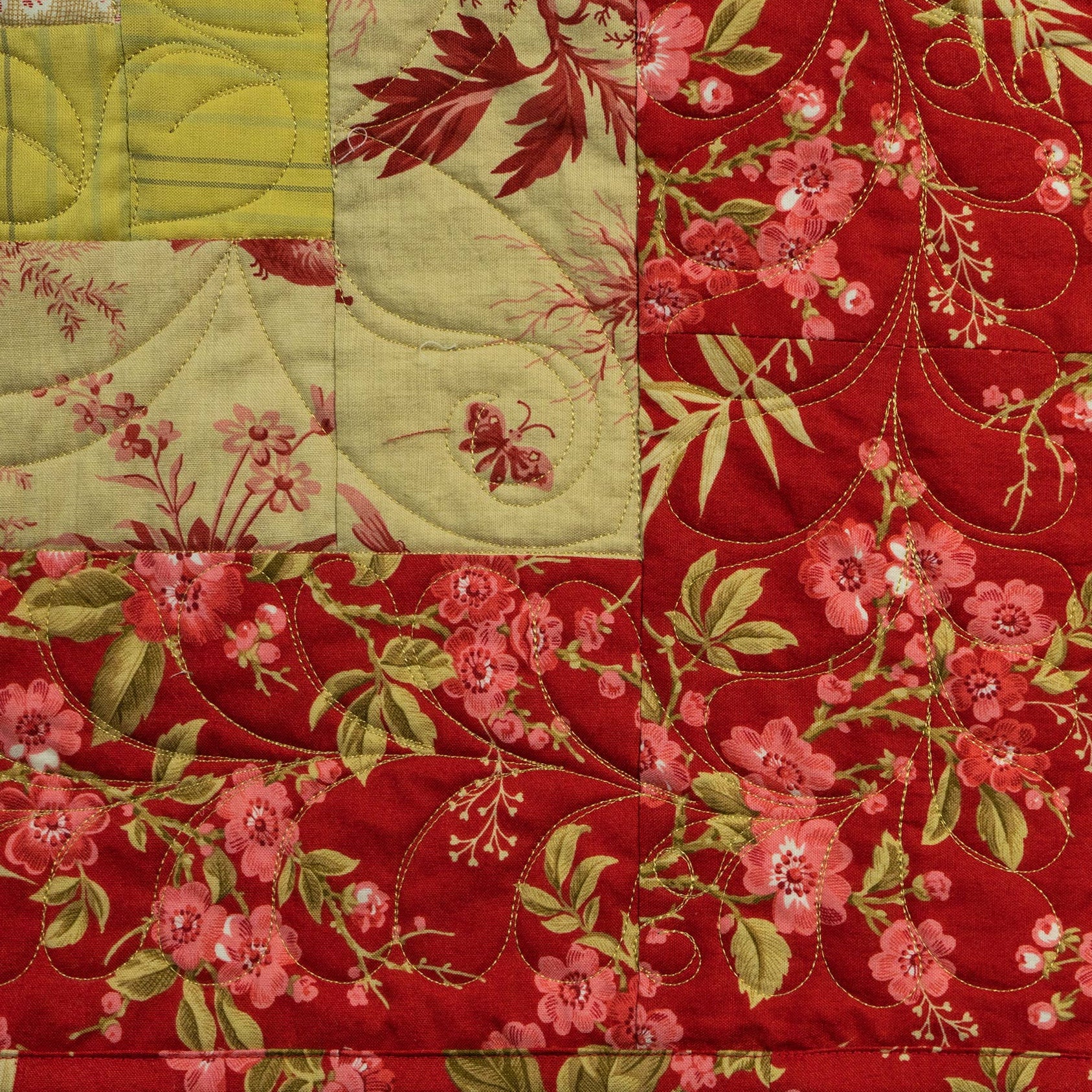Quilt with floral patterns in red, green, and pink on a red background