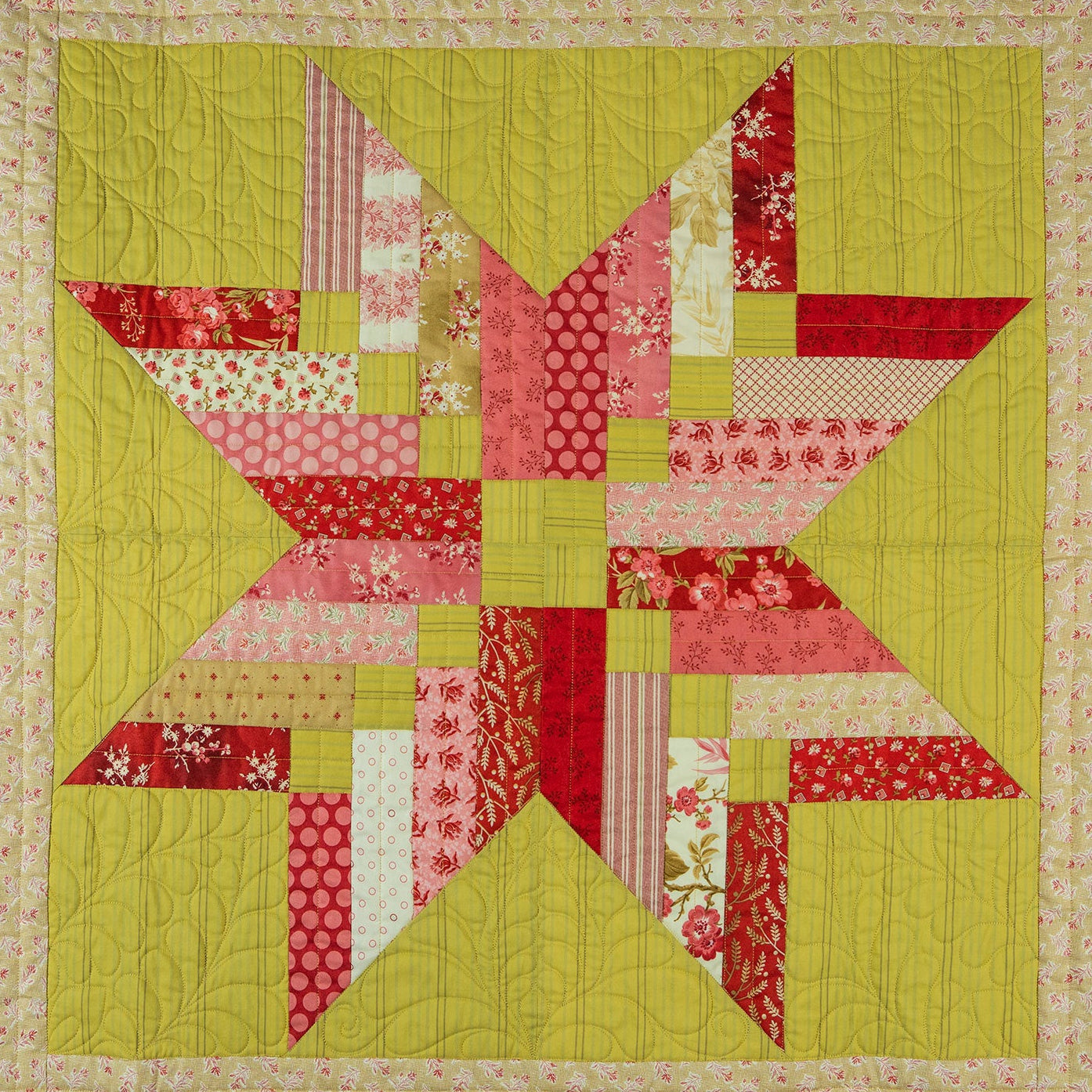 Patchwork quilt with a star design in red, green, and pink on a beige background