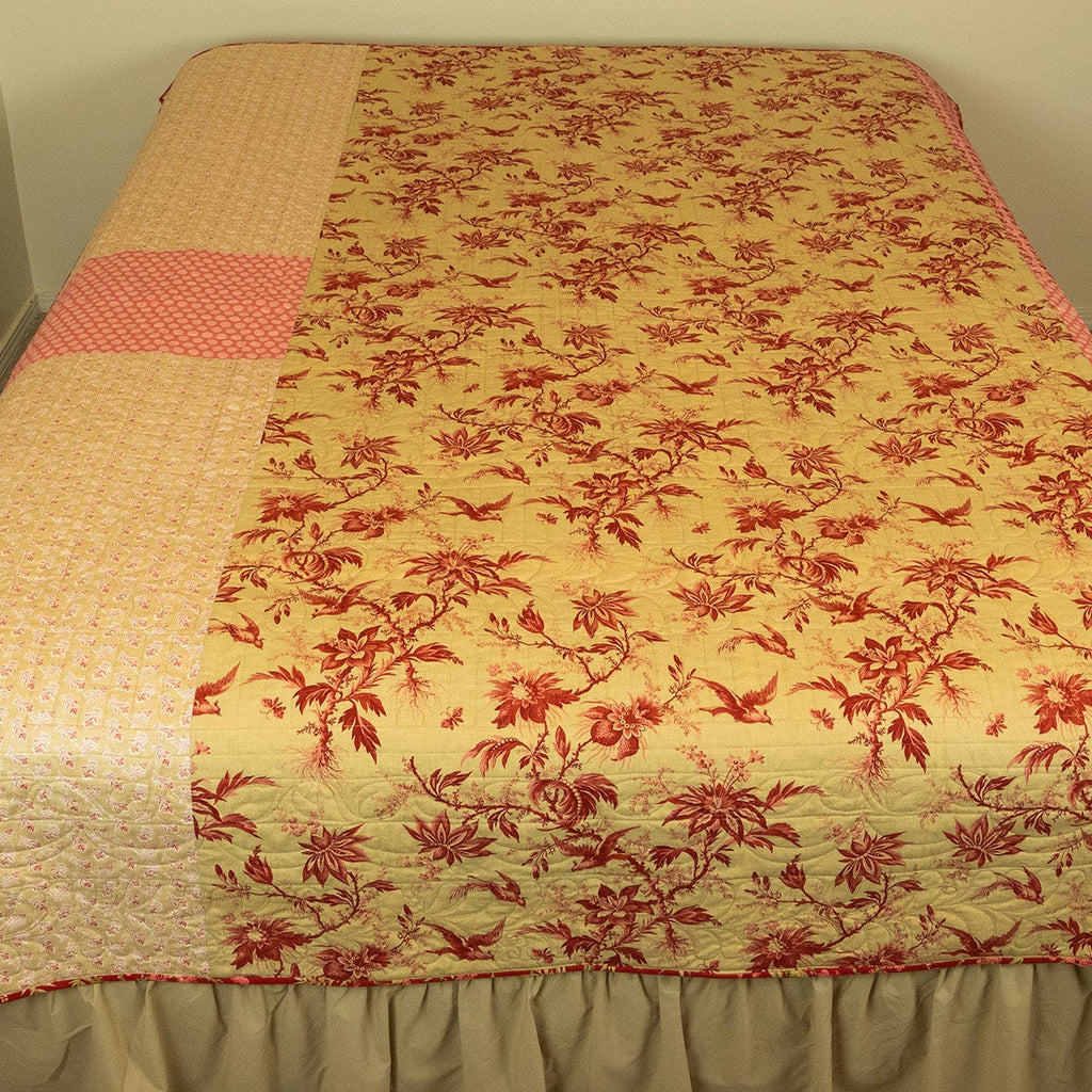 Floral quilt with red and beige pattern on a bed in a room.