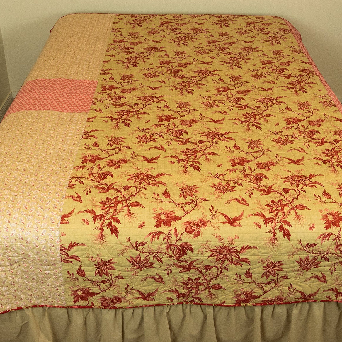 Floral quilt with red and beige pattern on a bed in a room.