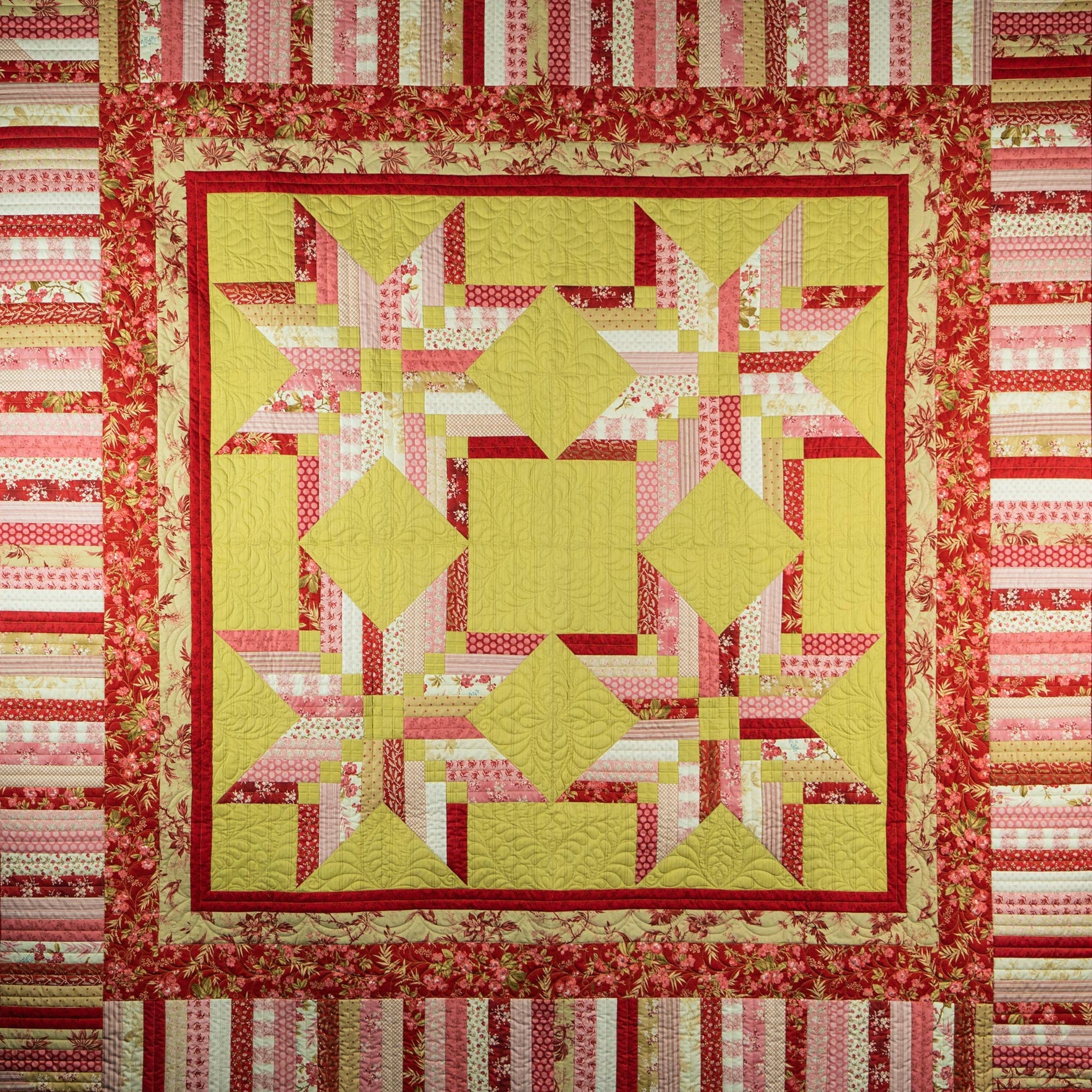 Quilt with geometric pattern in red, yellow, and pink on a striped background