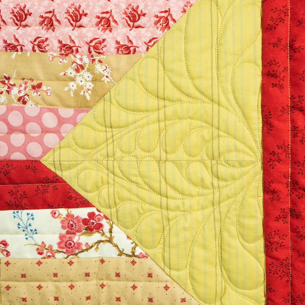 Quilt with floral and geometric patterns in red, yellow, and pink.
