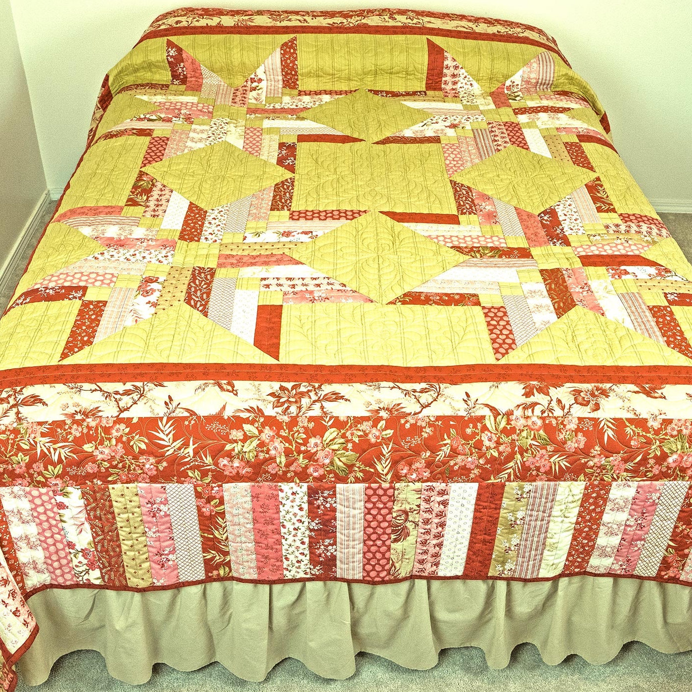 Patchwork quilt with red, yellow, and white patterns on a bed.