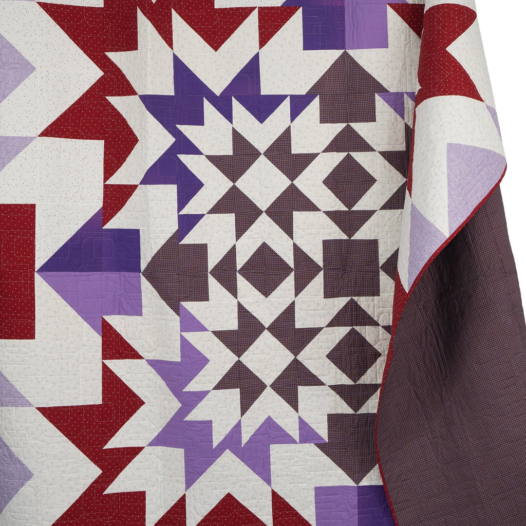 Quilt with geometric pattern in red, purple, and white on a white background