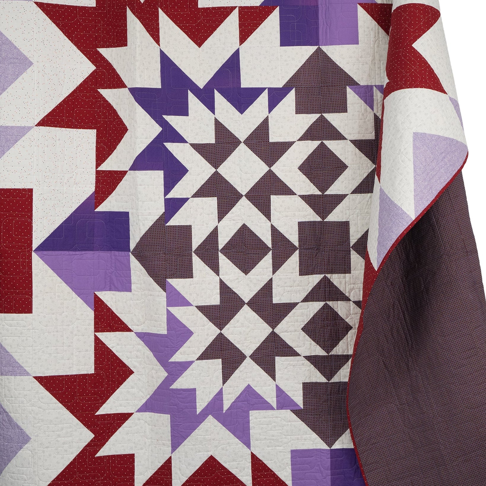 Quilt with geometric pattern in red, purple, and white on a white background
