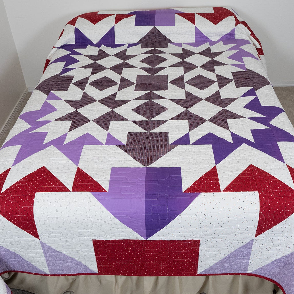 Colorful geometric quilt on a bed in a minimal room.