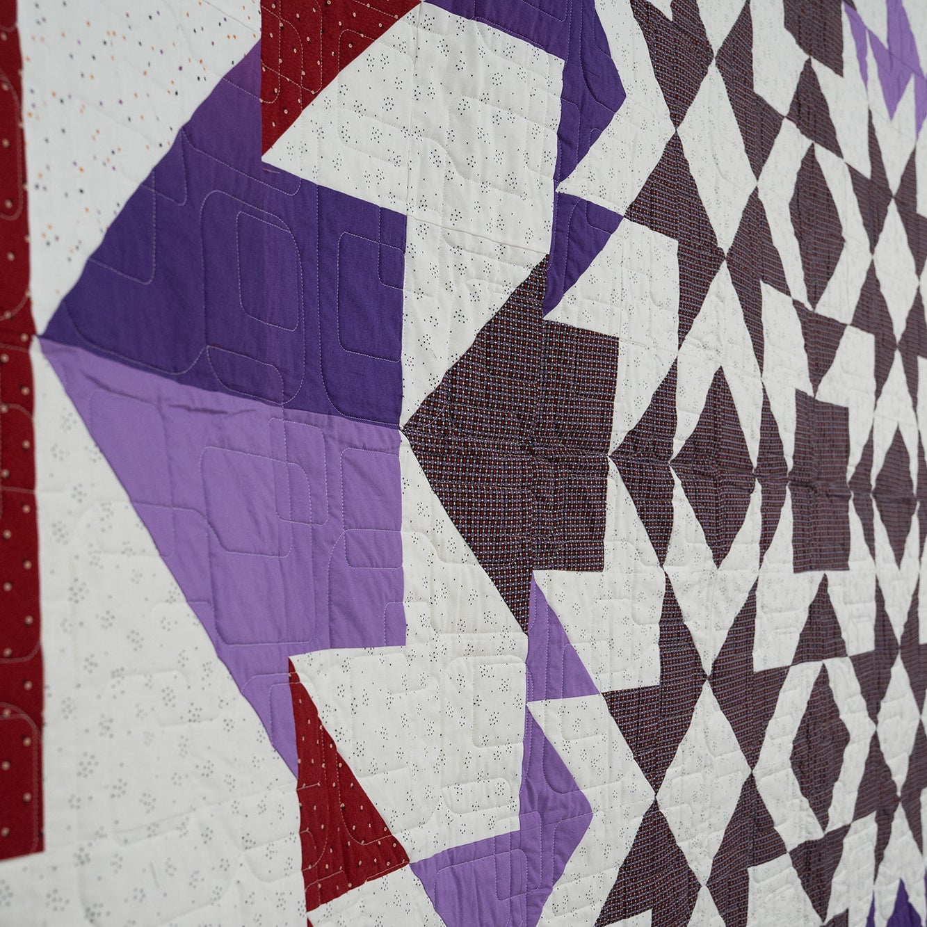 Close-up of a quilt with geometric patterns in red, purple, and white.