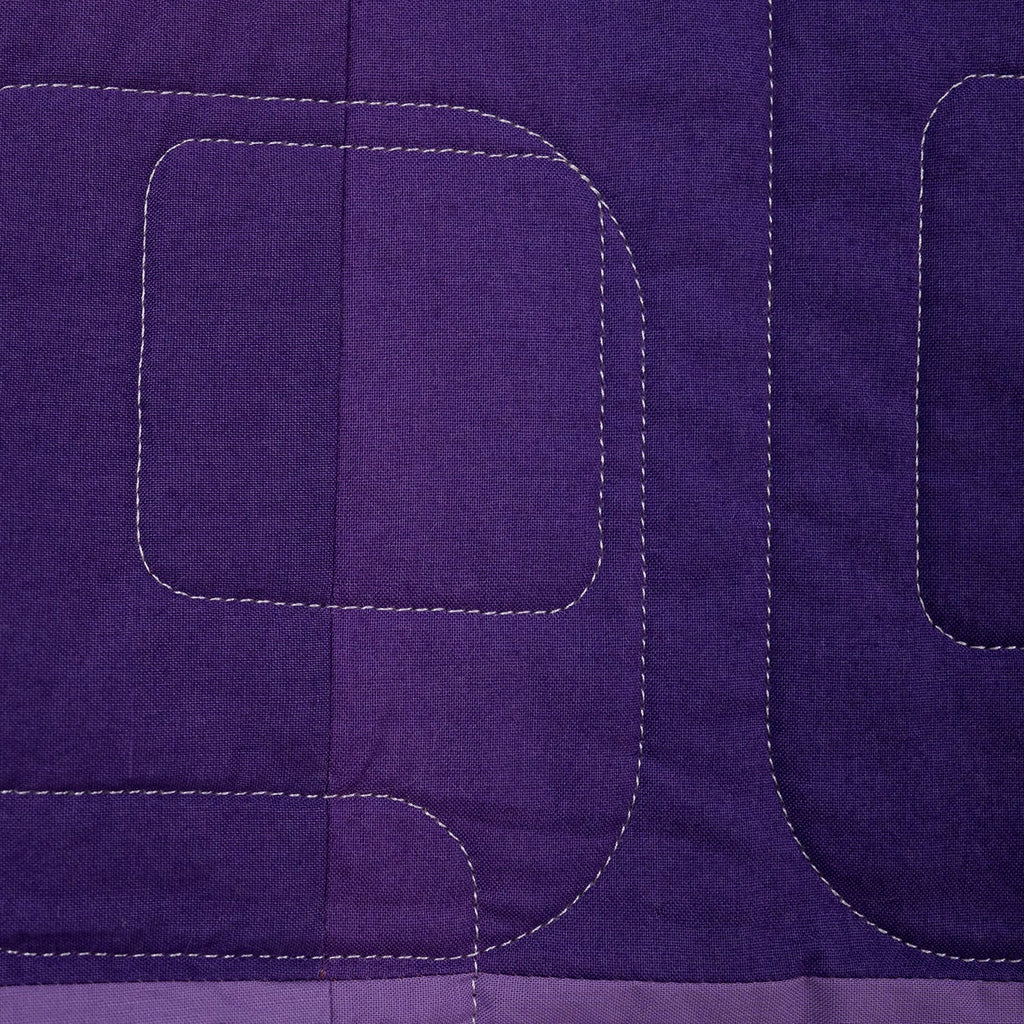 Close-up of a purple quilt with geometric stitching pattern