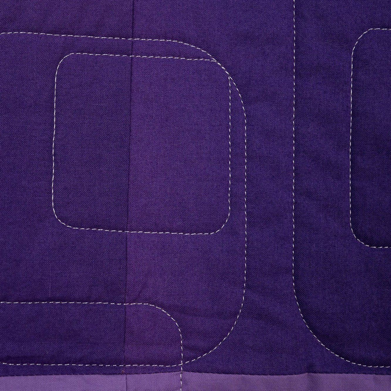 Close-up of a purple quilt with geometric stitching pattern