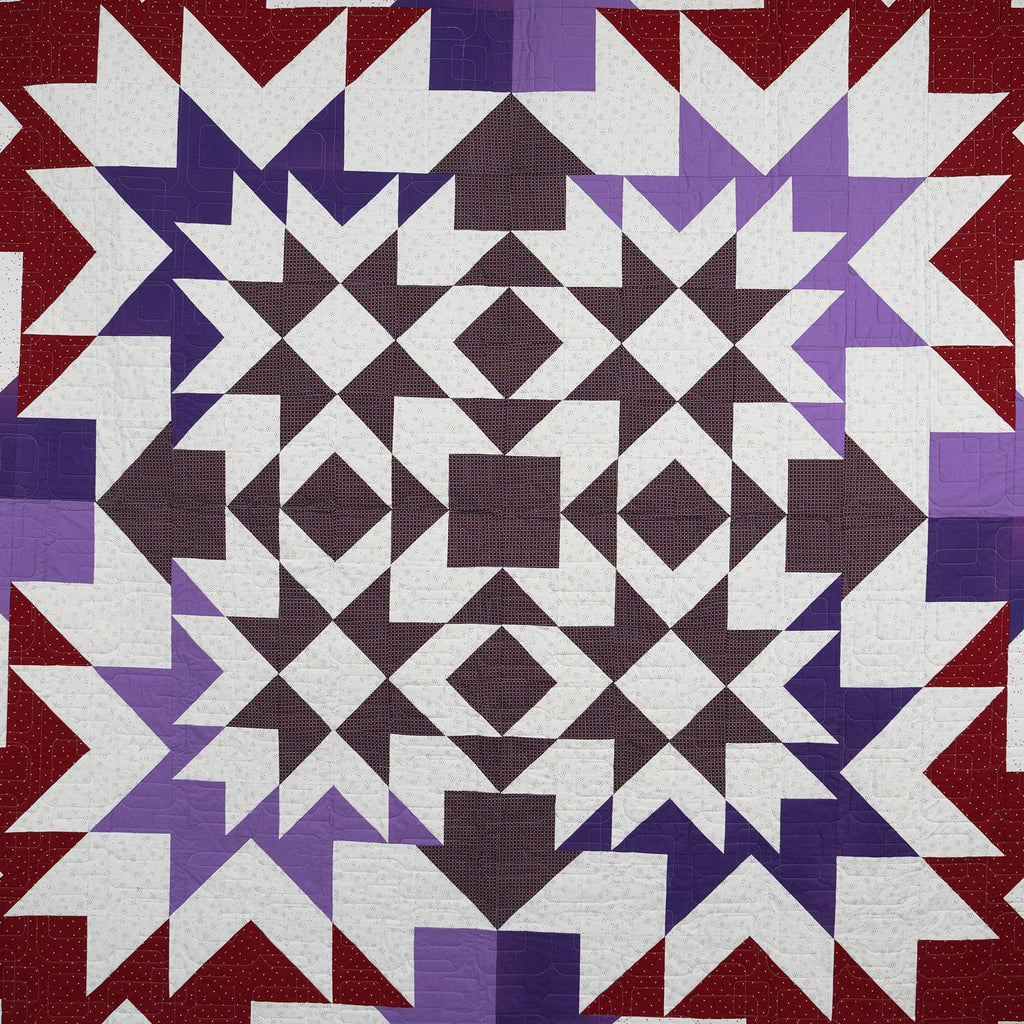 Quilt with geometric pattern in red, purple, and white on a white background
