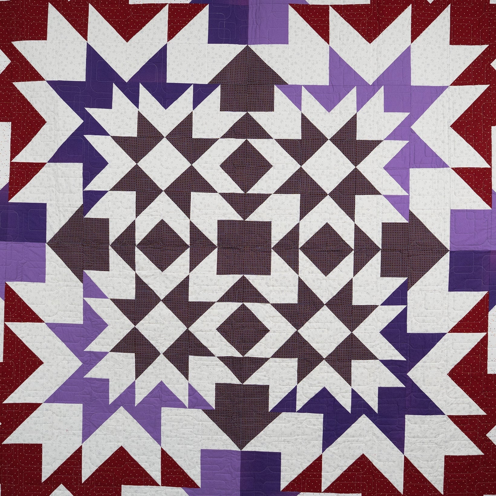 Quilt with geometric pattern in red, purple, and white on a white background